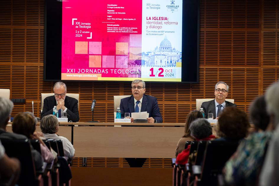 Three people sitting at a panel during a theological conference, in a lecture hall with an audience and a presentation screen in the background.