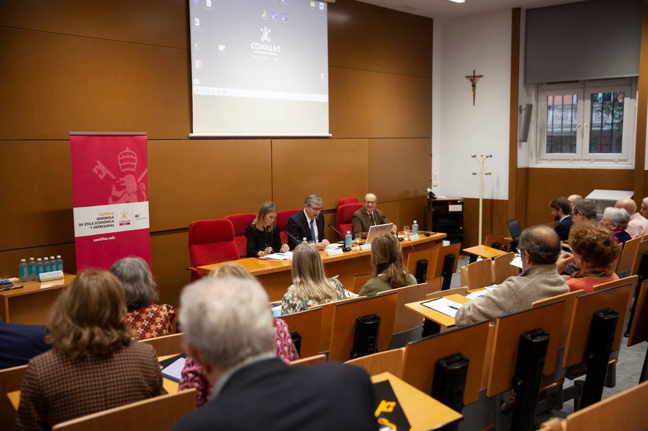 An academic panel session is taking place in a lecture hall with an audience listening.