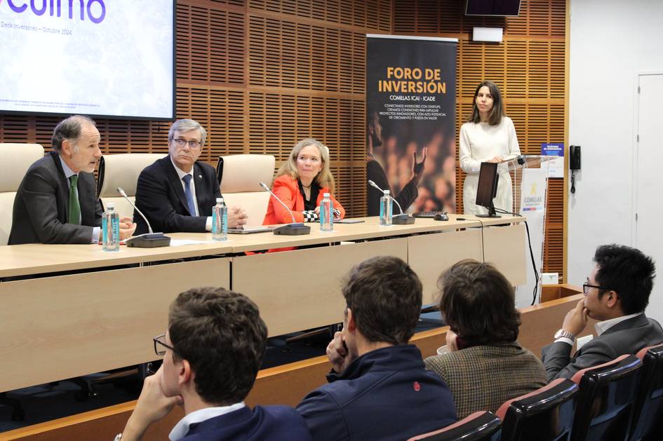 Una mujer está de pie dando una presentación en un foro de inversión ante un público y un panel de expertos sentados.