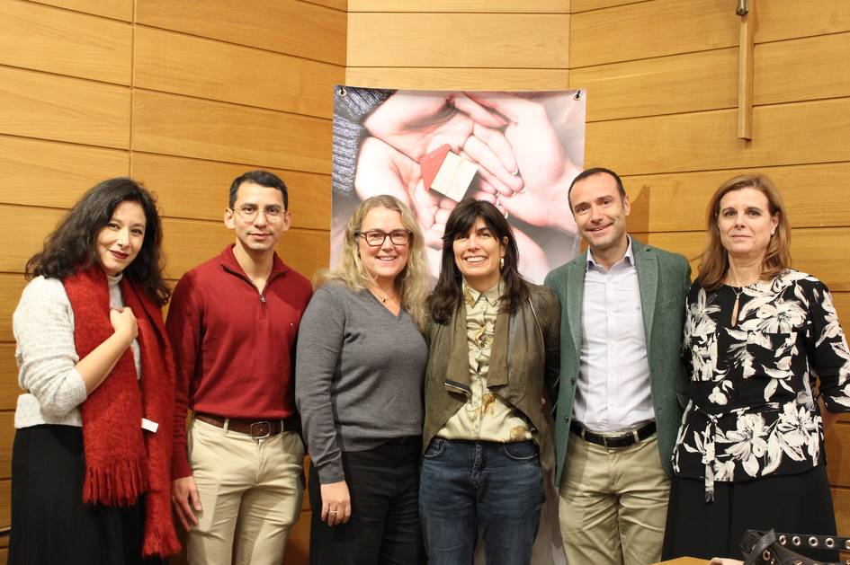 Un grupo de cinco personas sonríen para la foto en un evento en un salón con un póster de fondo.