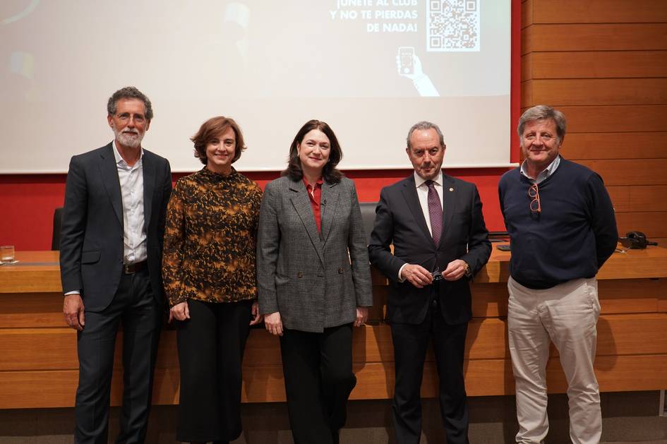 Cinco personas de pie en un auditorio frente a una pantalla con texto y código QR.