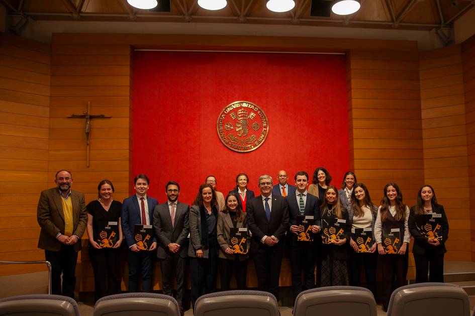 Un grupo de personas posando en una ceremonia formal frente a un fondo rojo con un emblema dorado.