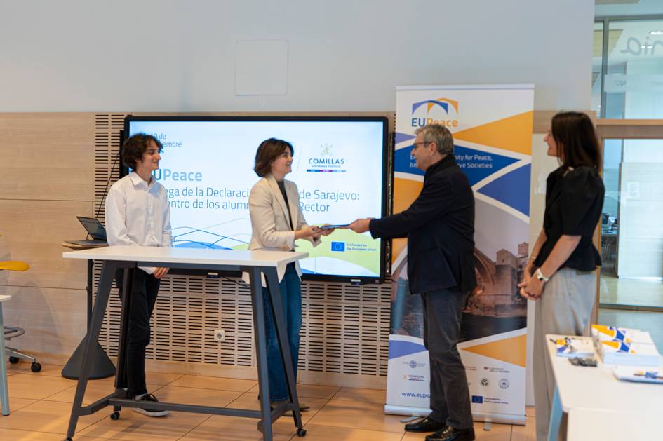 Un grupo de personas participa en un evento donde se firma un acuerdo relacionado con la paz y colaboración estudiantil.