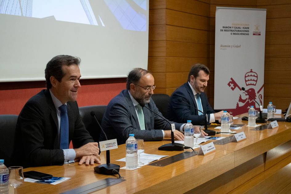 Tres hombres en una mesa durante un evento o conferencia en un salón moderno.