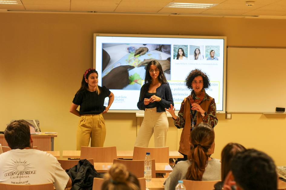 Three people presenting in a classroom with a projected slide in the background.