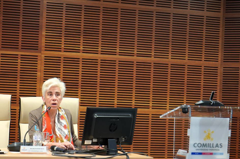 Una mujer de cabello blanco presenta en una conferencia mientras se encuentra frente a una computadora.