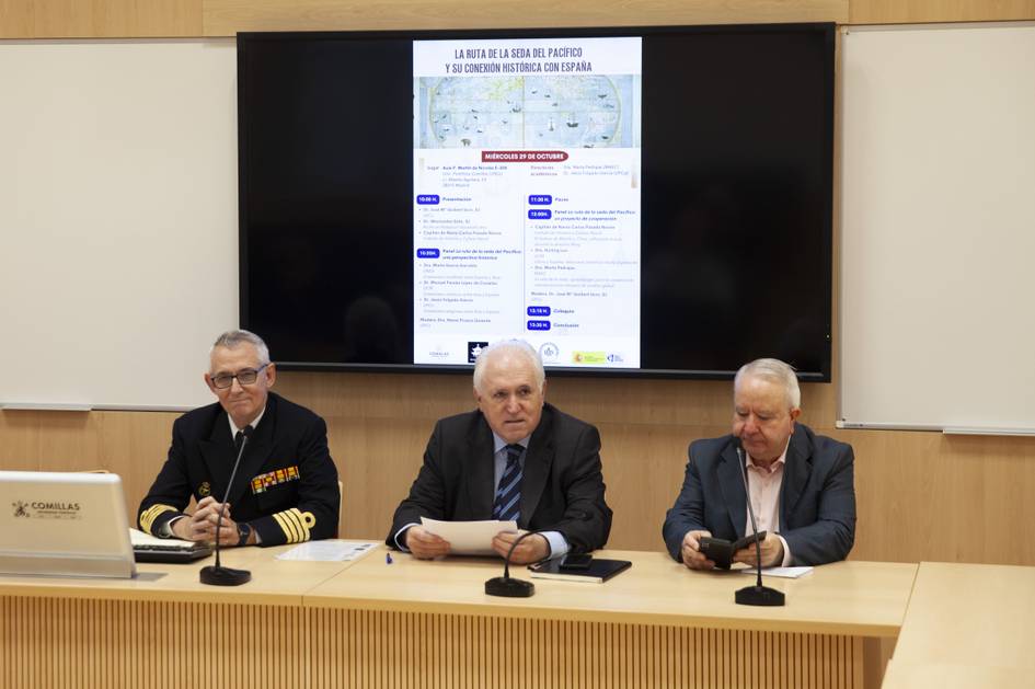 Tres hombres están sentados frente a una pantalla mostrando información en una sala de conferencias.