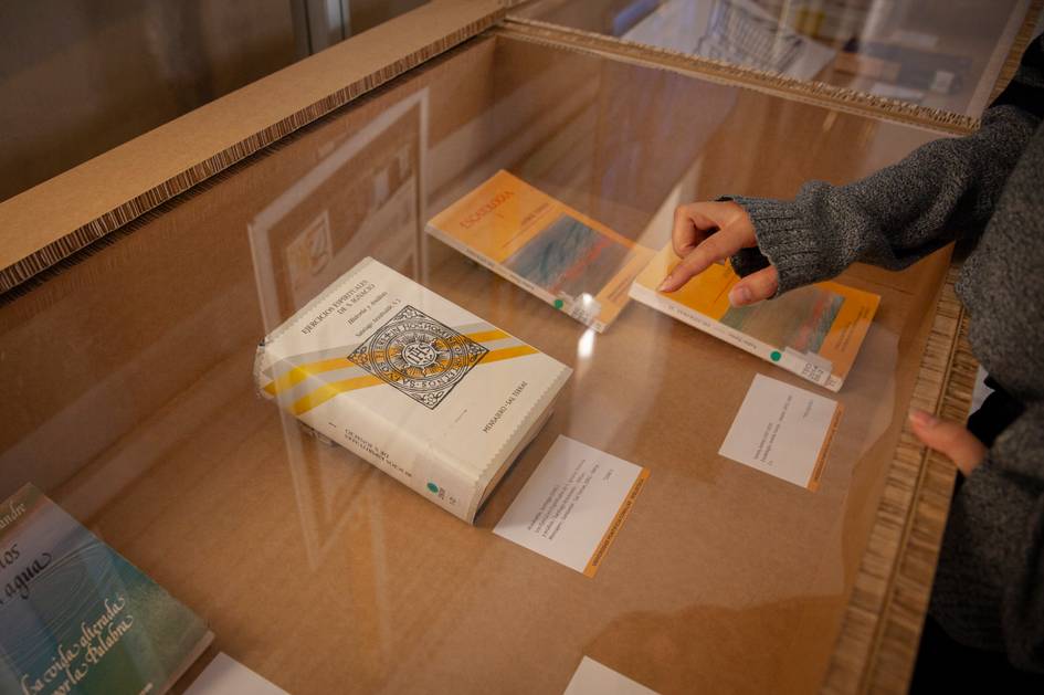 A person is pointing at a book displayed under a glass case in an exhibition.