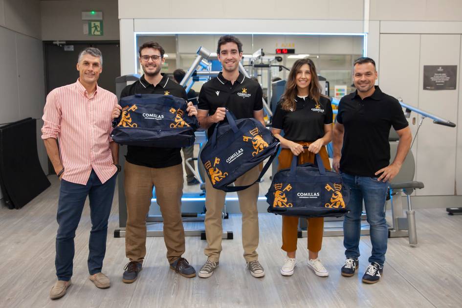 Five adults smiling and holding sports bags in an indoor setting.