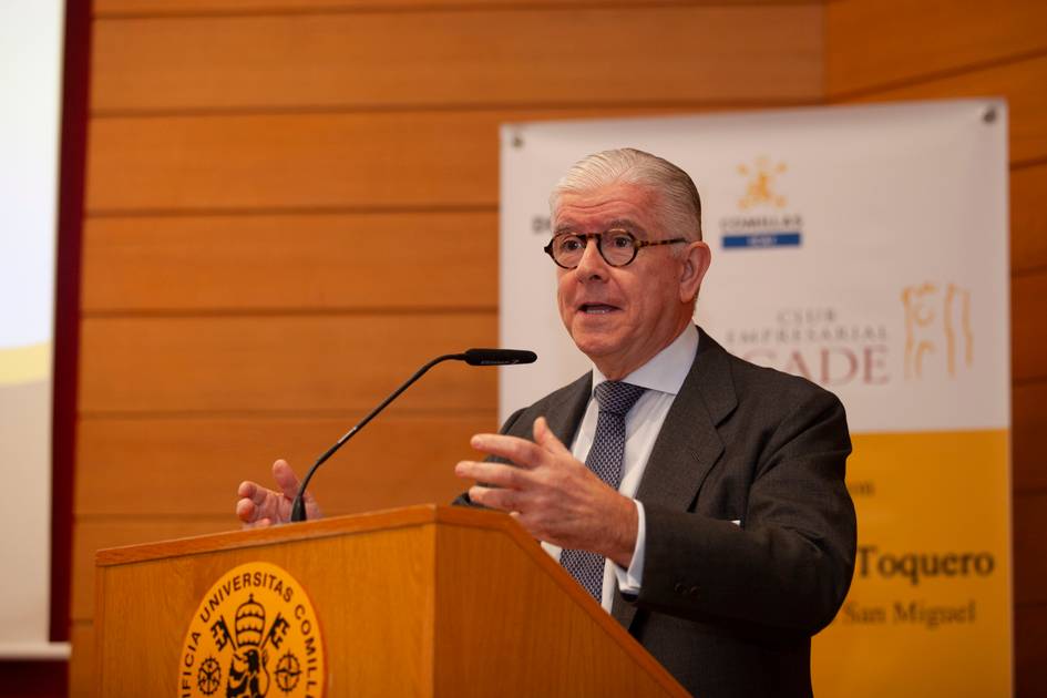 Un hombre mayor dando un discurso en un podio en un aula universitaria.