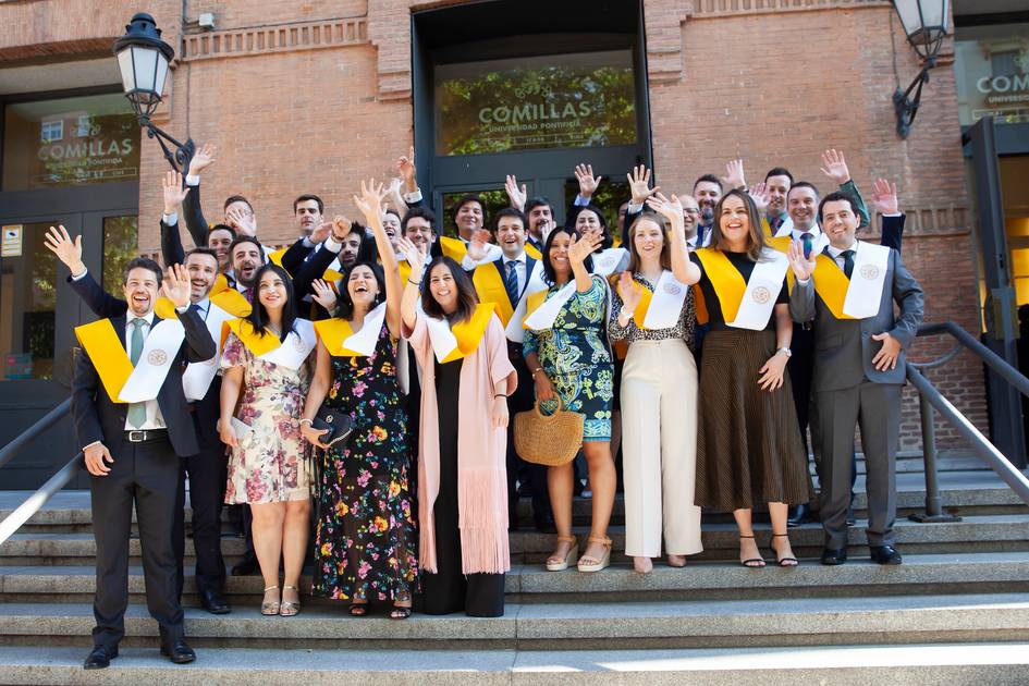 A group of graduates celebrating in front of a university building, waving their hands with joy.