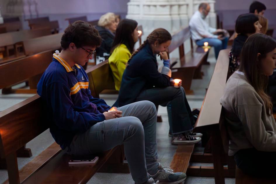 Young people sitting in church pews, some looking at their phones.