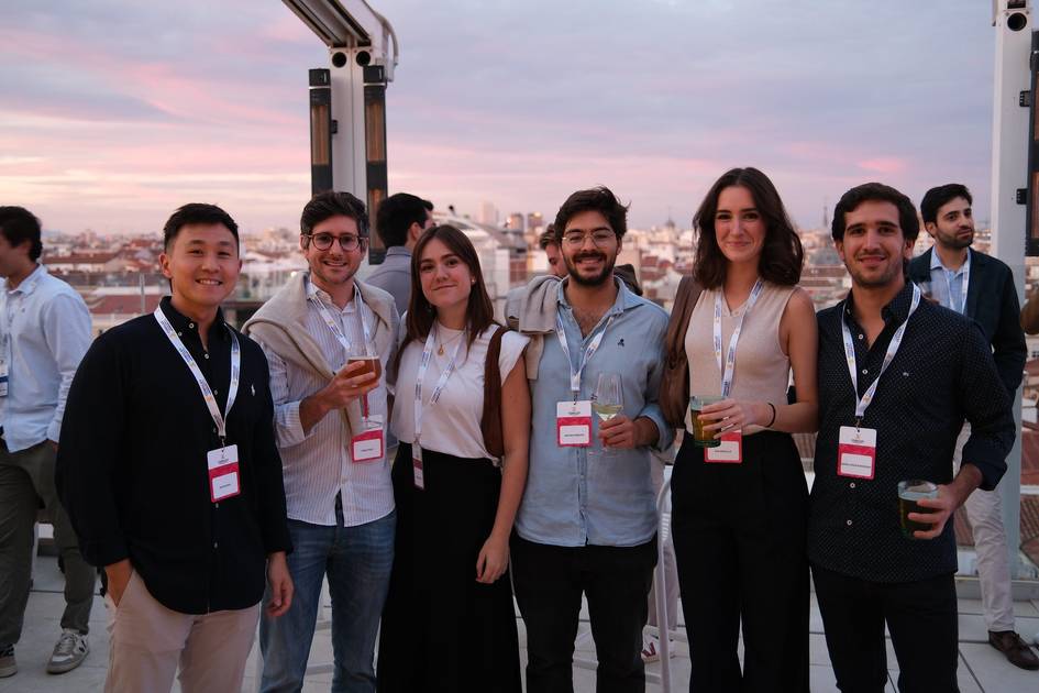 Grupo de seis personas disfrutando de una reunión al atardecer con bebidas en mano.