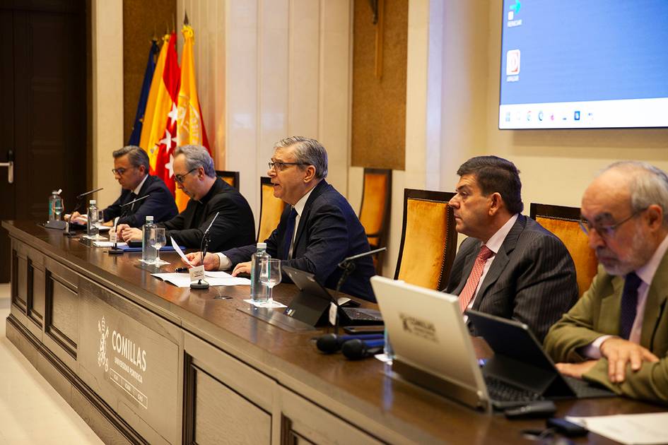 A group of five men sit at a long table during a formal meeting, with laptops and papers in front of them.