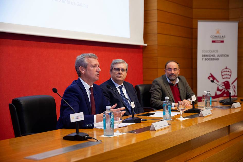 Three men in suits are seated at a conference table with microphones, participating in a panel discussion.