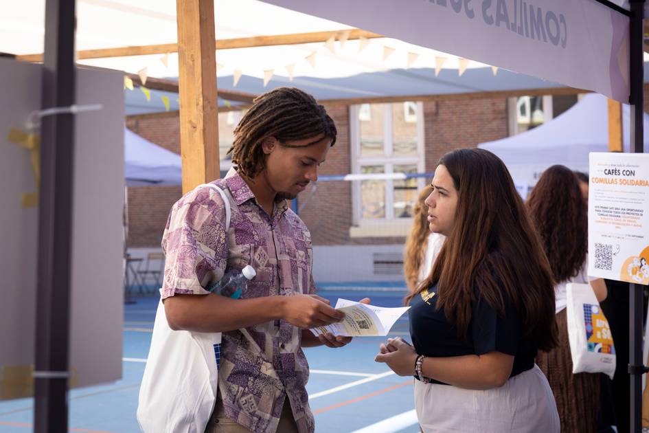 Dos jóvenes conversan en un ambiente al aire libre, rodeados de carpas.