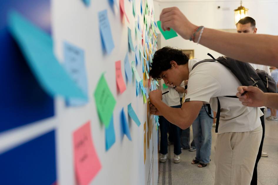 Un grupo de personas interactúa con una pared llena de notas adhesivas de colores.