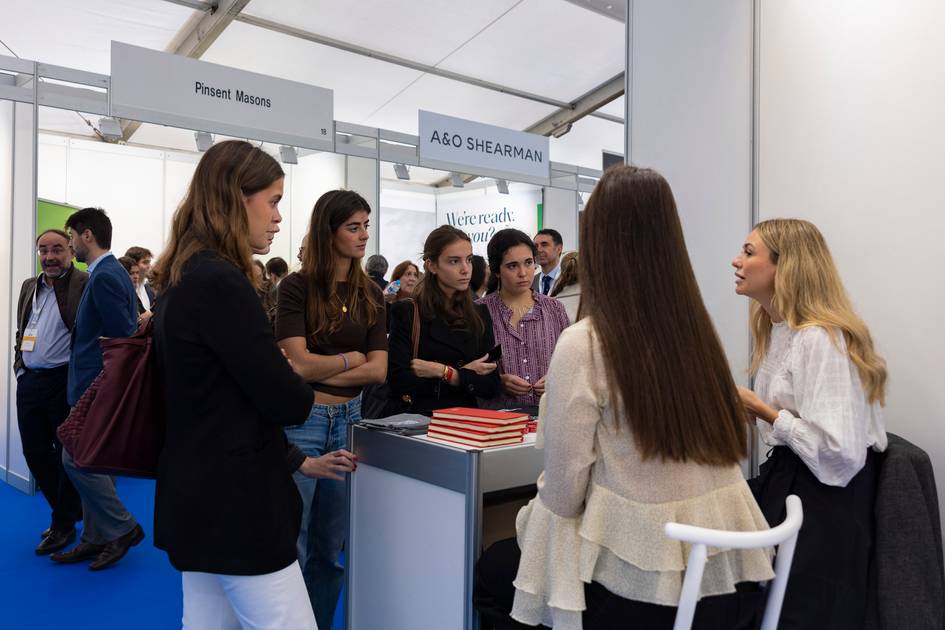 Un grupo de personas conversando en un evento o feria, con distintos stands al fondo.