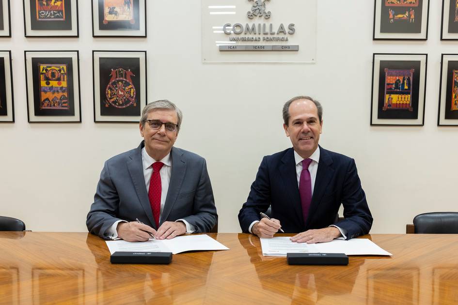 Dos hombres sentados en una mesa firmando documentos en un entorno académico.