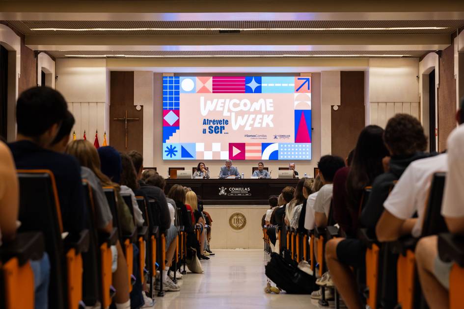 Un auditorio lleno de estudiantes en un evento de bienvenida con una pantalla que muestra un diseño colorido y el texto 'Welcome Week'.