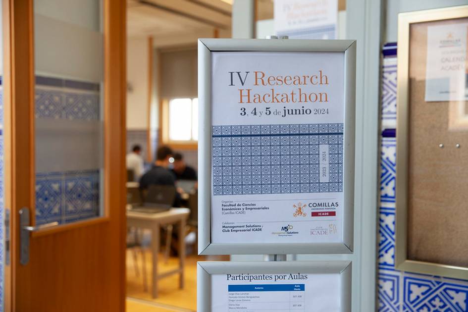 A poster for the IV Research Hackathon on June 3-5, 2024, displayed on a glass door with a partially visible academic setting in the background.