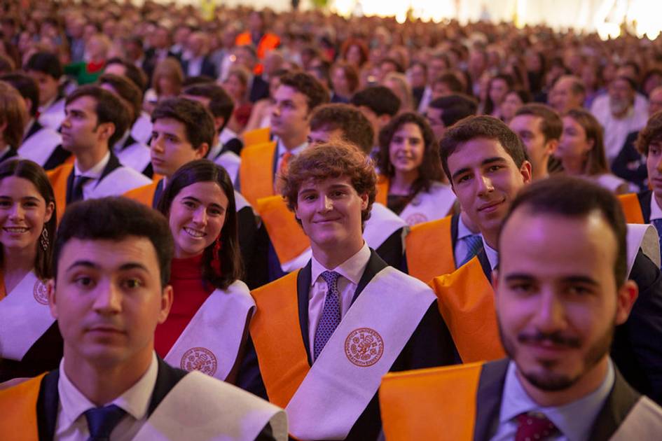 A group of young graduates in gowns and sashes at a graduation ceremony.