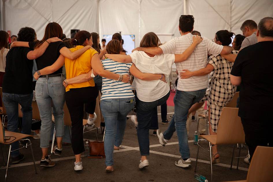 A group of people standing closely, linking arms around each other in a tented area.