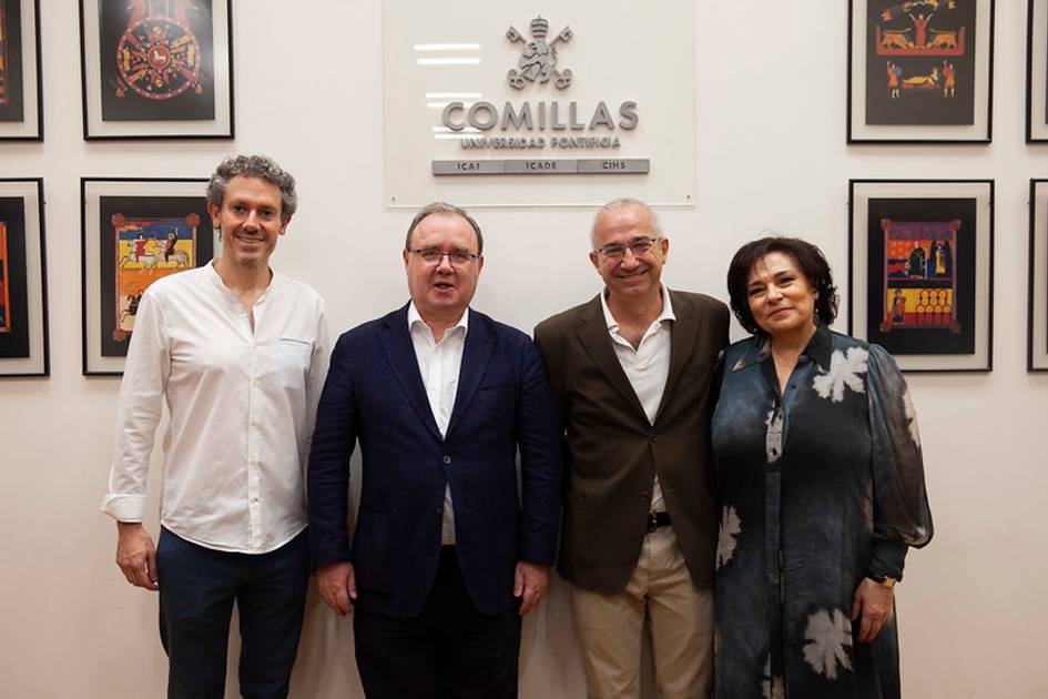 Four adults standing in front of a Comillas Universidad Pontificia sign and colorful artwork.