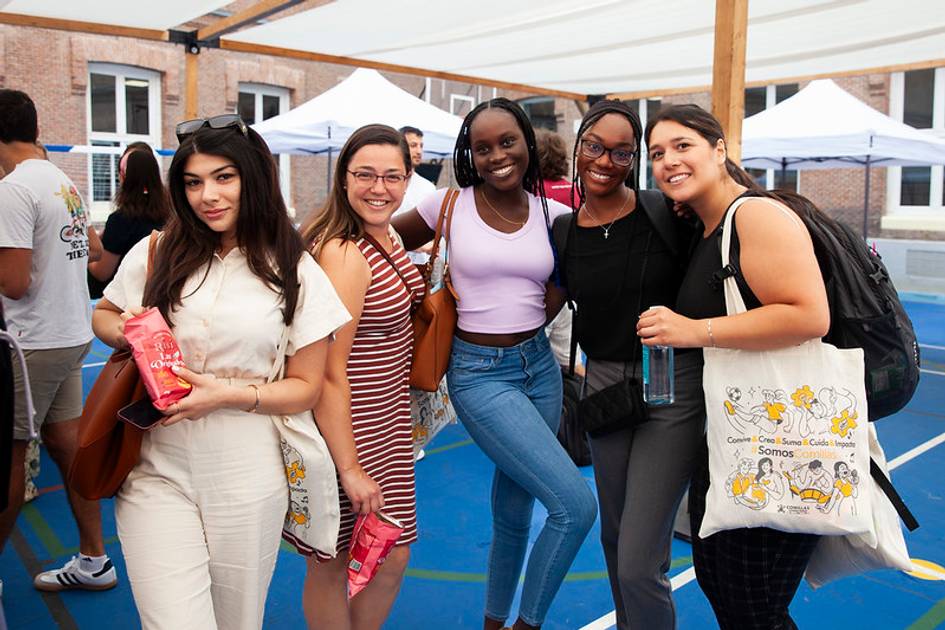 A group of five diverse young women smiling at a school event with snacks in their hands.