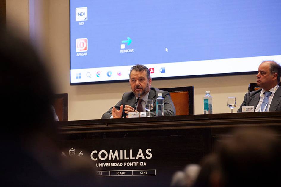 A man speaking at a podium in a conference room at Comillas Pontifical University