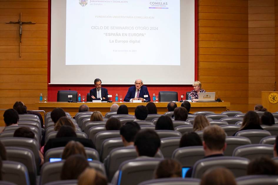 Tres personas se encuentran hablando en un panel frente a una audiencia en un salón de conferencias.