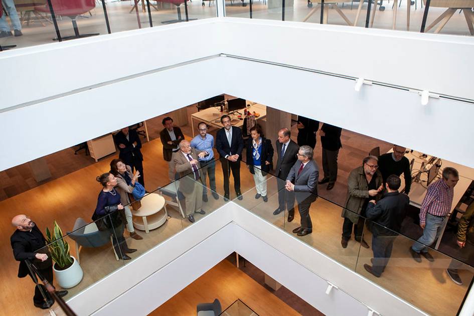 A group of people of various ages and genders in a modern office or event space, standing and conversing.