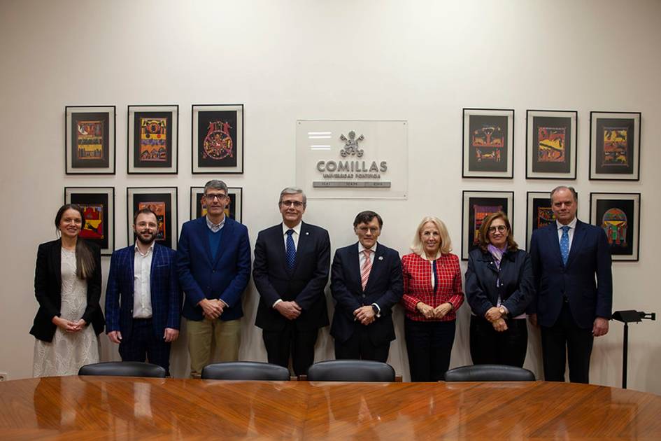 Grupo de siete personas de pie detrás de una mesa de conferencia dentro de una sala con cuadros en la pared.