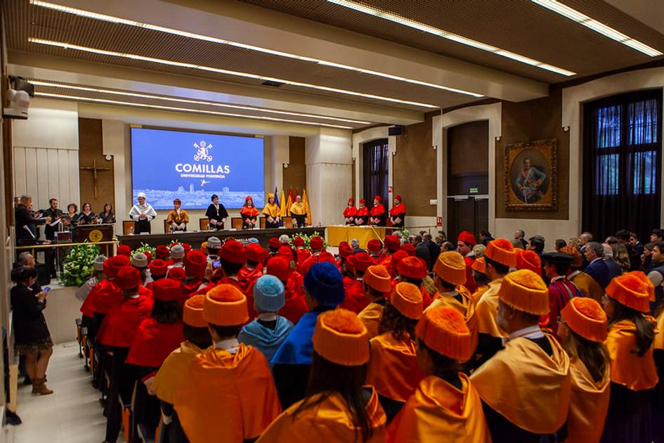 Ceremonia de graduación en un auditorio, donde los graduados llevan togas y birretes de colores y están de espaldas mirando hacia un panel de autoridades en el estrado.