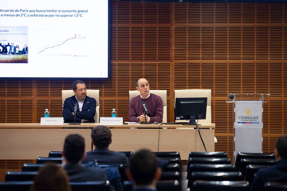 Dos hombres presentan en un seminario sobre el cambio climático ante una audiencia en una sala con paredes de madera.