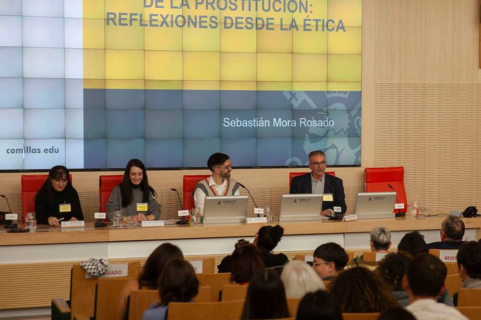 Cuatro personas participan en un panel de discusión en un evento académico sobre la ética de la prostitución.