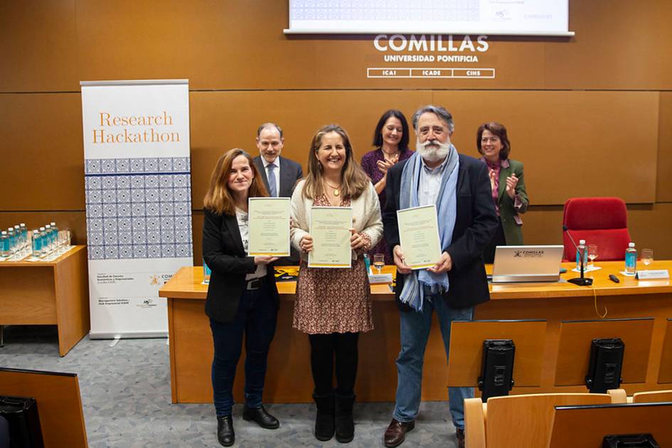 Tres personas sosteniendo certificados en un evento de la Universidad Pontificia Comillas.