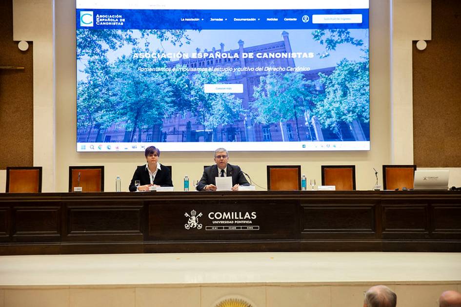 Una conferencia se lleva a cabo en un salón con pantalla que muestra un sitio web relacionado con la Abogacía.