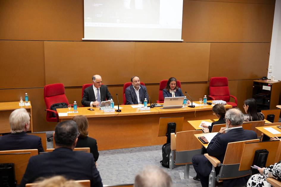 Una mesa de conferencias con tres ponentes y una audiencia en un ambiente académico.