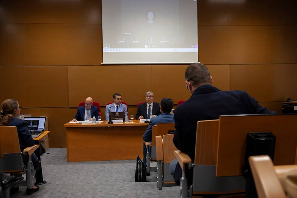 Una reunión en un auditorio con varios ponentes y asistentes sentados en filas.