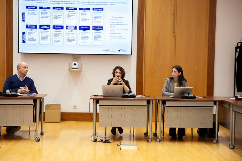 Una reunión de trabajo con tres personas sentadas frente a un proyector.