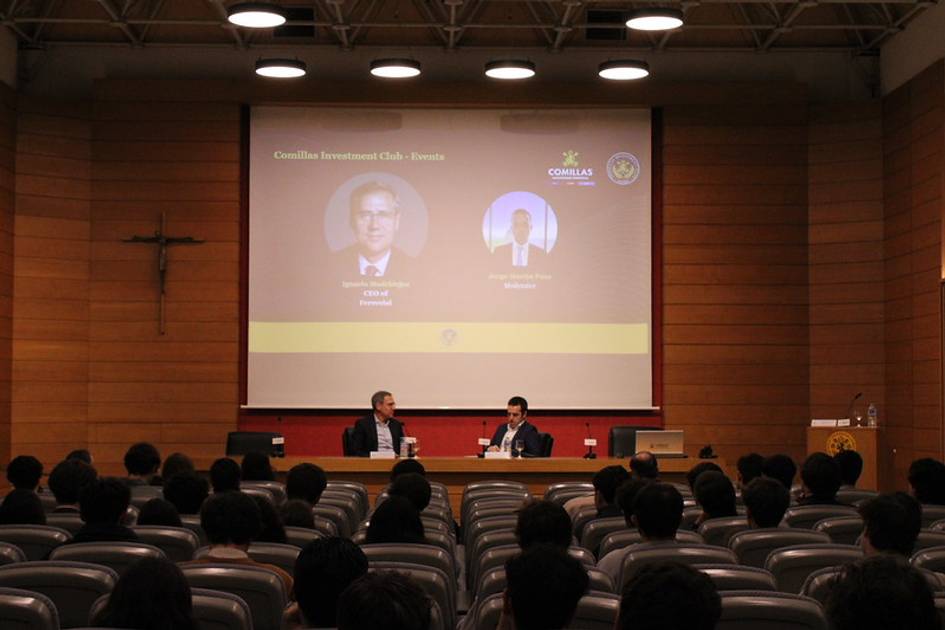 Una charla en un auditorio con dos oradores frente a un público atento.