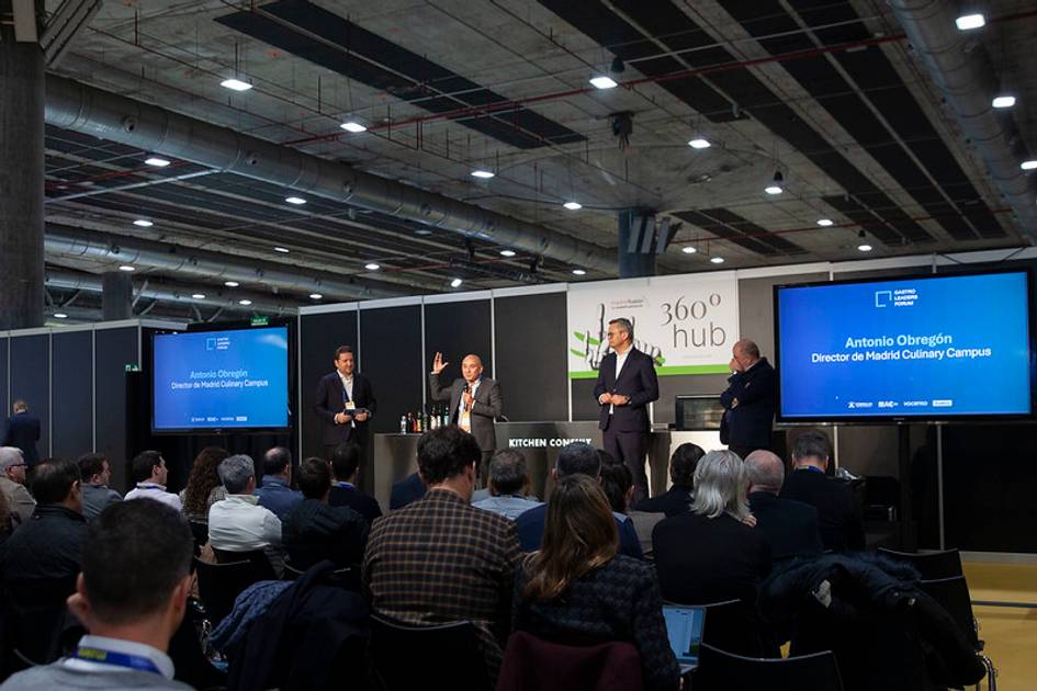 Un grupo de personas en un evento de presentación en un escenario con pantallas mostrando información.