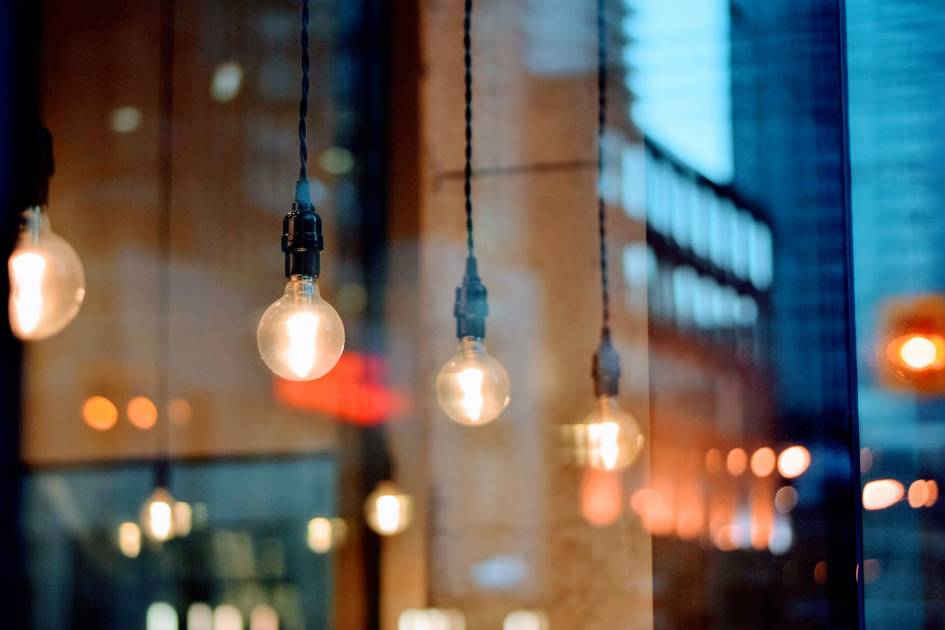 La imagen muestra bombillas colgantes iluminando un ambiente urbano reflejado en una ventana.