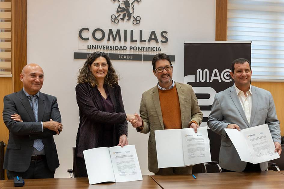 Un grupo de cuatro personas firmando documentos en un evento en la Universidad Pontificia Comillas.