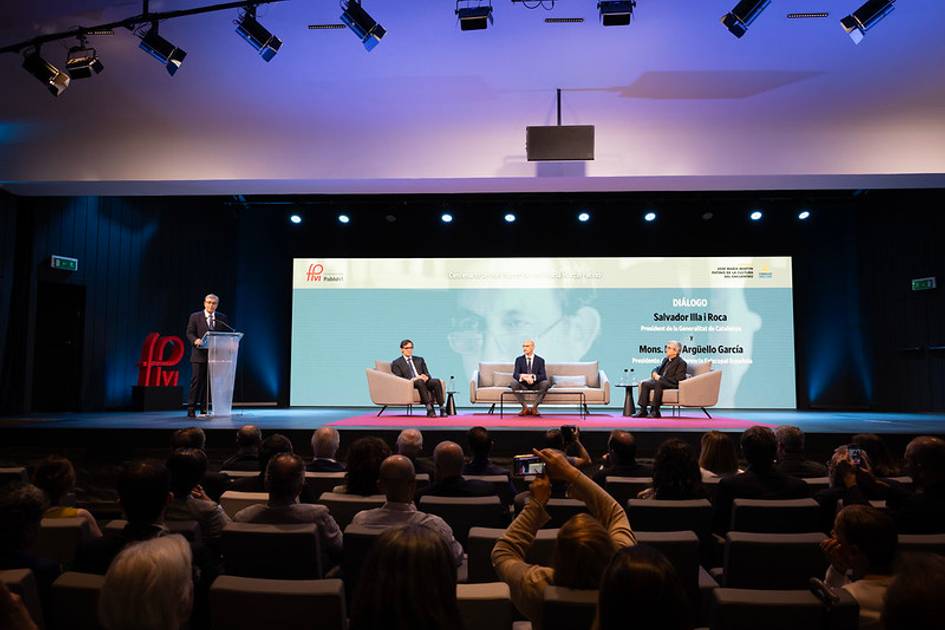 Un evento con varias personas sentadas en un escenario mientras un orador se dirige a la audiencia.