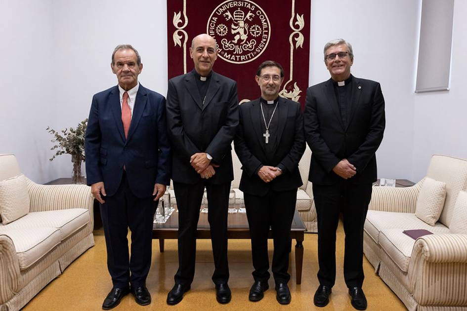 Cuatro hombres de pie en un ambiente formal, vestidos de traje y con hábitos religiosos, posando para una fotografía.