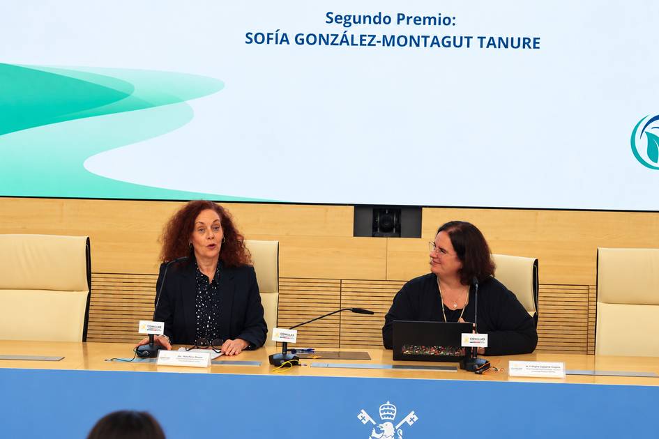 La imagen muestra a dos mujeres durante una ceremonia de premiación en un salón con pantallas y un ambiente formal.