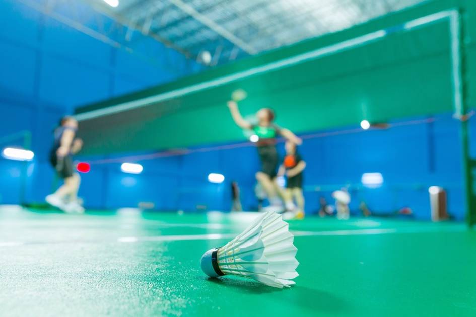 A close-up view of a shuttlecock on a green badminton court with players in the background.