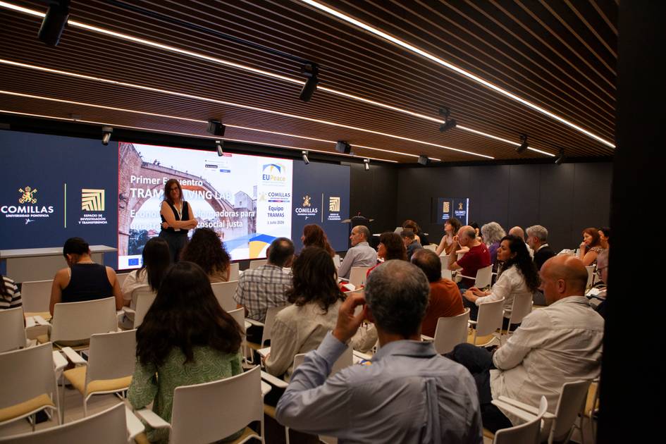 Una conferencia en un auditorio con un gran grupo de personas escuchando a una ponente.